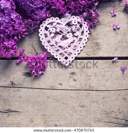 Background with fresh  violet lilac flowers and pink decorative heart on aged  wooden planks. Selective focus. Place for text. Square image.