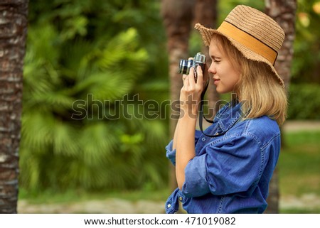 Charming young happy smiling woman taking pictures in a wild tropical forest. Young photographer, tourist.