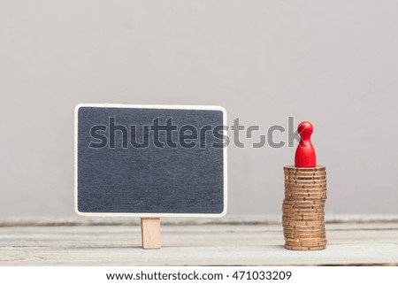 a square blackboard sign (empty, copyspace) next to a stack of eurocents with red pawn on a wood table. grey background, studioshot.