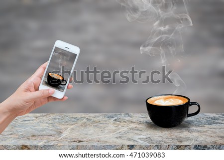 Woman hand holding and using mobile,cell phone,smart phone photography and redolent cappuccino coffee on stone floor with blurred image of wood texture. abstract background.