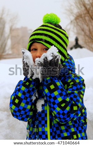 Happy little boy laughing and playing with snow. The child keeps the snow in his hands