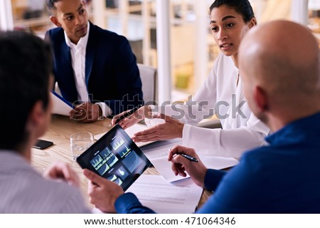 Business meeting between four upper management board members in the new modern office conference room with technology integrated in the form of an electronic tablet. Royalty-Free Stock Photo #471064346