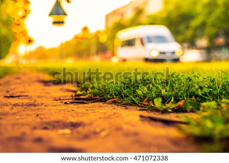 Sunset in the city, the car rides on the road. Close up view from the path level of the lawn, image in the orange-blue toning