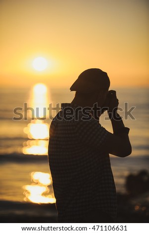 Silhouette of young photographer on the beach takes pictures of the sunset over the sea.