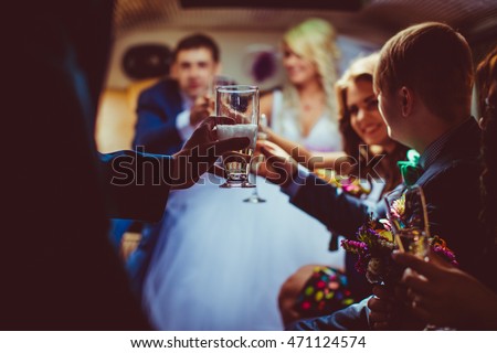 People clang glasses with champagne while sitting in the limousine