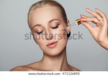 Young pretty Woman getting special skin treatment at beauty salon. Beautiful Girl applying eye serum. Closed eyes. Isolated on gray background. Smooth skin without wrinkles. Royalty-Free Stock Photo #471126890