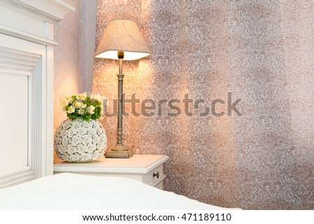 Bedroom interior in cream color.bouquet of white flowers and table lamp on  bedside table. vertical photo