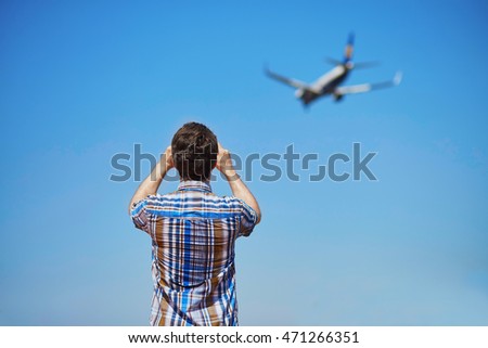 Man is looking at the glide path and landing plane or taking a photo of it. Aircraft spotting concept