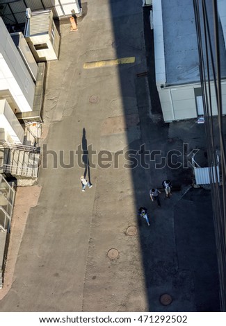 man goes on an asphalt road against buildings and cast a long shadow of man, silhouette of man in sunshine and three more people near building in shadow, top view, high resolution