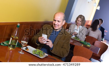 Smiling mature man taking pictures of dinner with smartphone in restaurant

