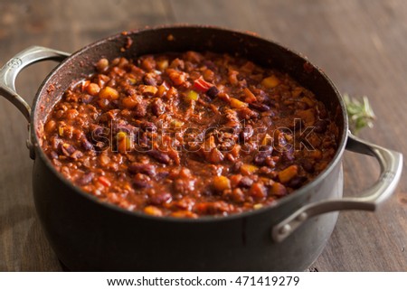 Organic Vegetarian Chili In Iron Pot Served With Rosemary On Distressed Wood Country Table. Royalty-Free Stock Photo #471419279