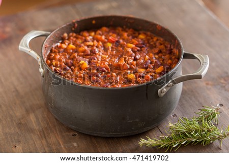 Organic Vegetarian Chili In Iron Pot Served With Rosemary On Distressed Wood Country Table.