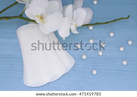 Sanitary pads and lilac orchid on the blue wooden background. Woman hygiene protection
