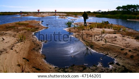 Oil?s pipe-line in the Sakhalin. Blue puddle, sandy bank covered grass by day. Silhouette of man in the distance.