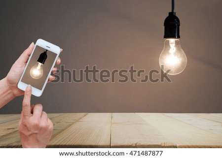 Woman hand holding and using mobile,cell phone,smart phone photography and wooden floor with old light bulb on dark background is concrete wall for background. copy space.