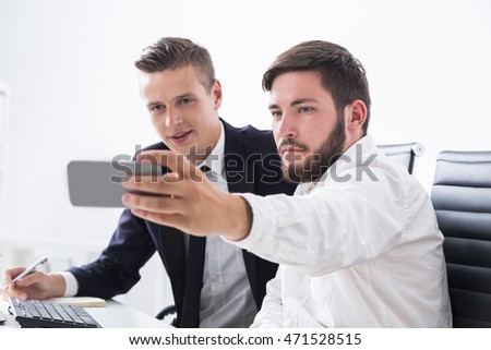 Two businessmen taking selfie at workplace while sitting at computer table. Concept of leisure time at work and importance of short breaks for productivity