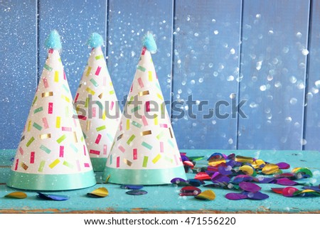 Party hat and colorful confetti on wooden table. Glitter overlay