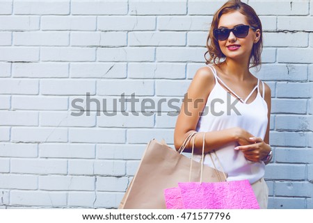 Pretty young woman holding shopping bags against a brick wall