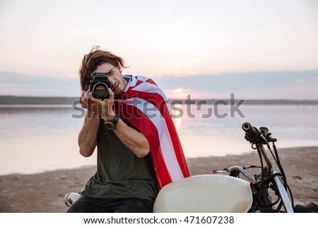 Young man making photo with camera while sitting on his motocycle outdoors