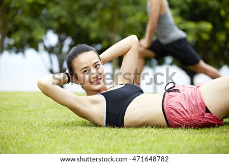 young asian woman doing sit-ups on grass in city park.