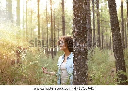 Young girl looking up and listening to the pine trees in a forest behind a tree while wearing casual clothing