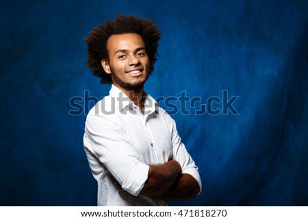 Young handsome african man with crossed arms over blue background.