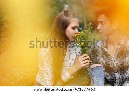 Loving couple teens together. Girlfriend and boyfriend together. The boy looks at the girl. Girl smelling a bouquet of wildflowers. Creative shooting. First love. He falls in love. Date.