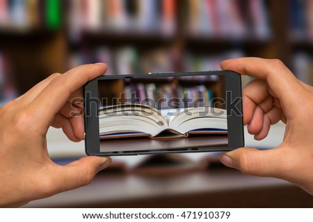 Woman hands with mobile cell phone to take a photo of open book on the table in library
