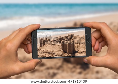 Woman hands with mobile cell phone to take a photo of sand castle on the sea shore