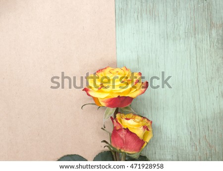 Red and yellow roses on wooden background. Blank sheet of paper, copy space. Flower mockup