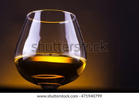 Snifter glass with brandy standing on a wooden table over a yellow lit background
