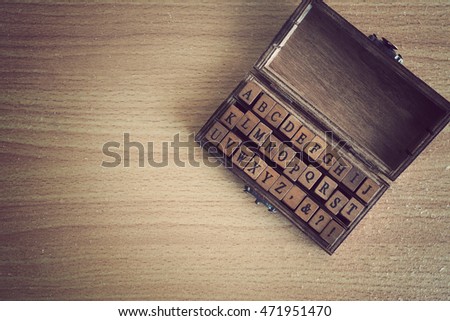 Alphabets stamp in the box on wooden background. Toned image.