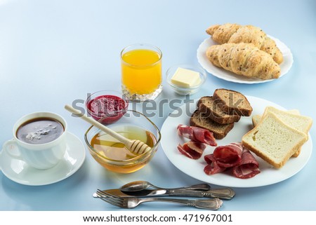 Delicious breakfast. Served with butter, orange juice, jam, honey, croissants, knife, fork. Yellow, blue. Blue background. Horizontal image