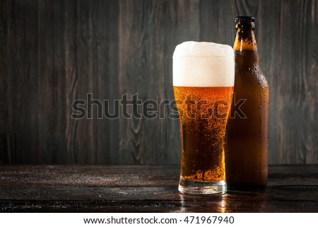 Glass of beer and beer bottle on wooden background
