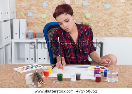 Woman painter at work in college office. Cork board on wall. Palette and paint lie on desk. Concept of higher education in art and sculpture. 