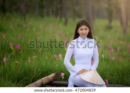 Beautiful vietnamese girl in traditional dress (ao dai) in a park with beautiful pink flower background