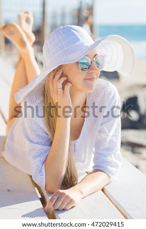 Pretty woman in white dress and hat relaxing on the beach at the sea background 