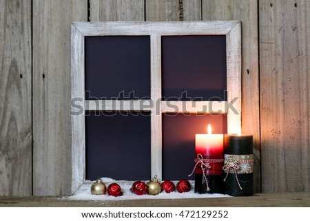 Blank rustic window with red and green Christmas candles, snow, and gold and red ornaments by antique weathered wood background