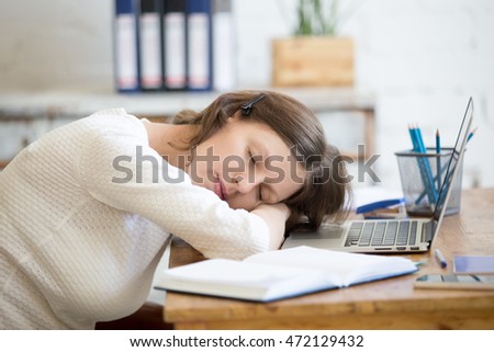 Portrait of young woman lying on the table in front of laptop, sleepy, tired, overworked or lazy to work. Attractive business woman napping in home office relaxing after work on laptop computer