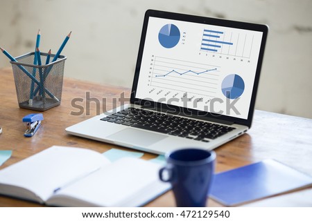 Home office interior in loft space. Workplace with wooden table, office supplies, documents, organizer and laptop. Modern office workplace. Focus on laptop screen with charts and diagrams