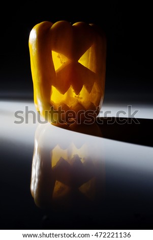 Food art creative concept. Halloween scary face carved into yellow capsicum vegetables   with back light over a dark background.