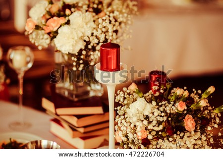 Wine red candles stand on high white holders between the bouquets