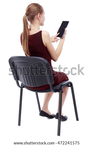 back view of woman sitting on chair and looks at the screen of the tablet.  Rear view people collection.  backside view of person.  Isolated over white background. A girl in a burgundy dress sitting