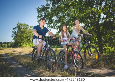 Happy young family with cute daughter cycling at meadow