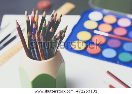 Artwork workplace. Blank white paper, colorful pencils, watercolor palette with paint brushes, ruler, sharpener on a grey wooden table. Back to school concept. Toned picture.