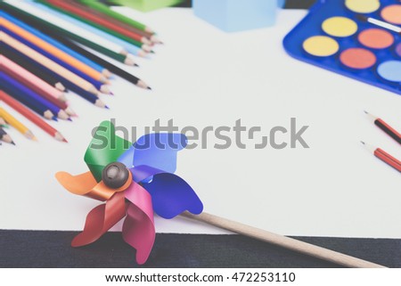 Artwork workplace. Blank white paper, colorful pencils, watercolor palette with paint brushes, ruler, sharpener and windmill toy on a grey wooden table. Back to school concept. Toned picture.