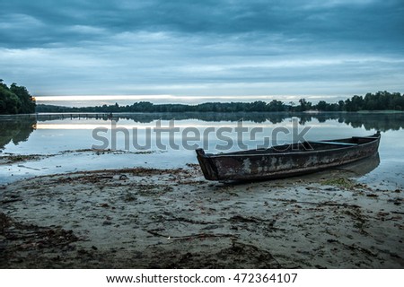 Lake view with boat. The wood boat on lake at sunset. Concept of loneliness, lacking direction, no leadership, rudderless, floating, listless or generally adrift without a goal. stillness calms Royalty-Free Stock Photo #472364107