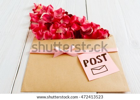 Romantic post message with flower petals, closeup. Floral composition of rose bloom and kraft paper on white wooden background, romantic present