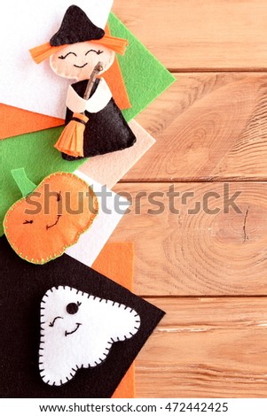 Halloween cute felt ornaments. Home made small witch with broom, pumpkin head, ghost. Halloween crafts, colored felt pieces on wooden background with blank space for text. Autumn kids crafts 