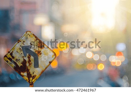 Old curve road warning sign on blur traffic road with colorful bokeh light abstract background. Copy space of transportation and travel concept. Retro tone filter color style.